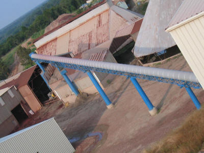 Overhead, covered and 30" wide x approximately 250' long, troughed transfer conveyor set on mono columns to give unobstructed access below.